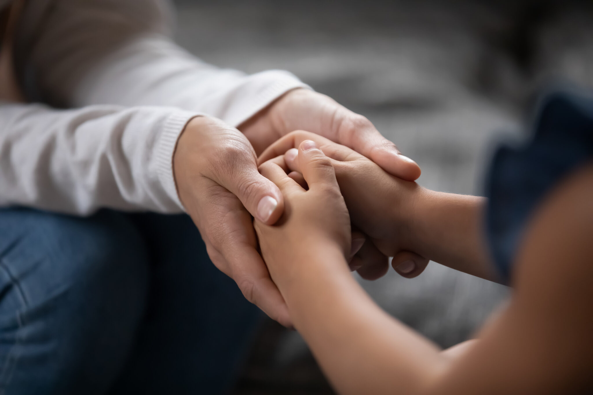 An adults holding the hands of a child lovingly.