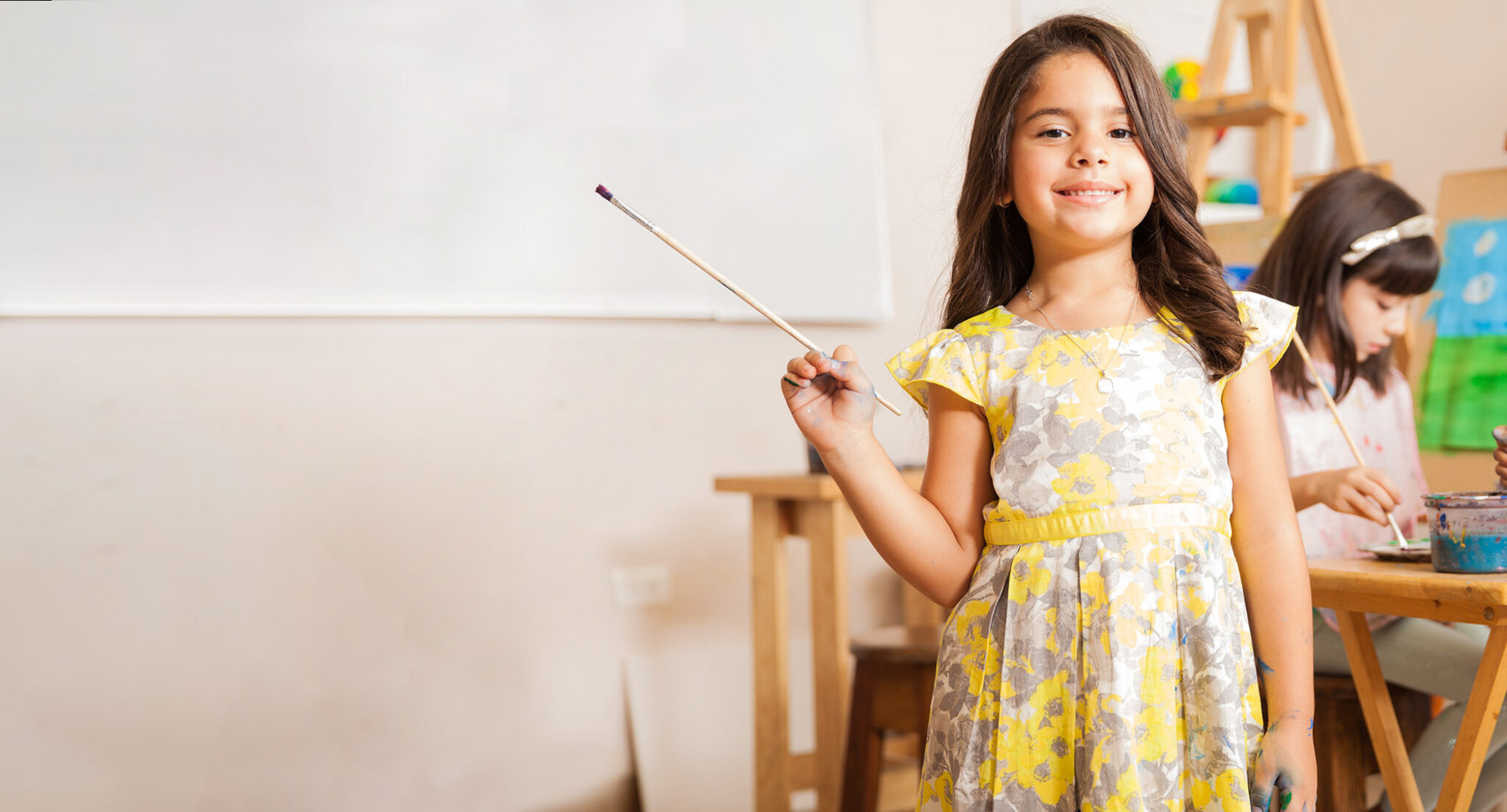 happy girl in school holding paintbrush