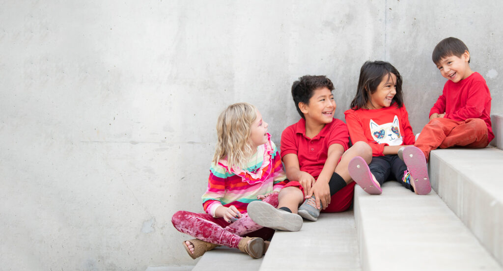 Four children sitting on concrete stairs laughing together