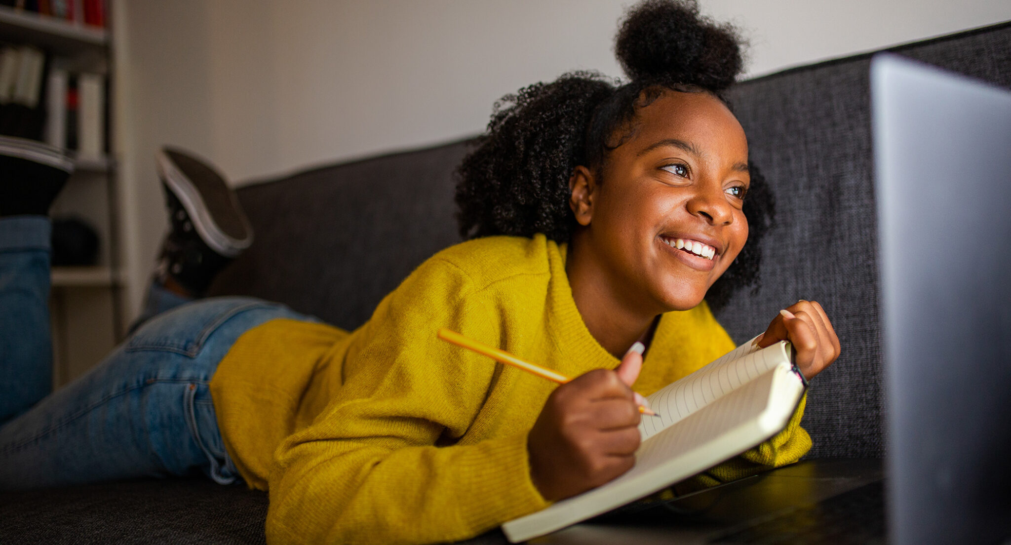 African American teenage girl doing her homework on a couch, smiling.