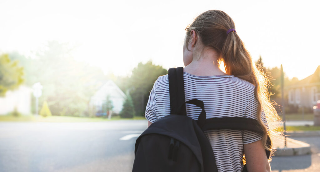 Teenage girl wearing backpack walking outside.