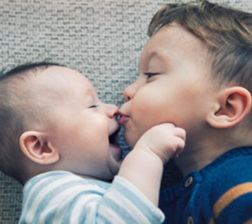Little boy kissing his baby brother on those making them laugh.