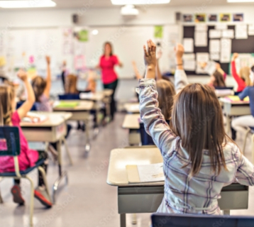 Children raising their hands in an elementary school classrom.