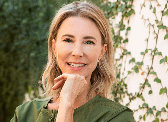 Darcy Olsen, founder and CEO of the Center for the Rights of Abused Children, smiling and posing with a hand on her chin, surrounded by greenery.