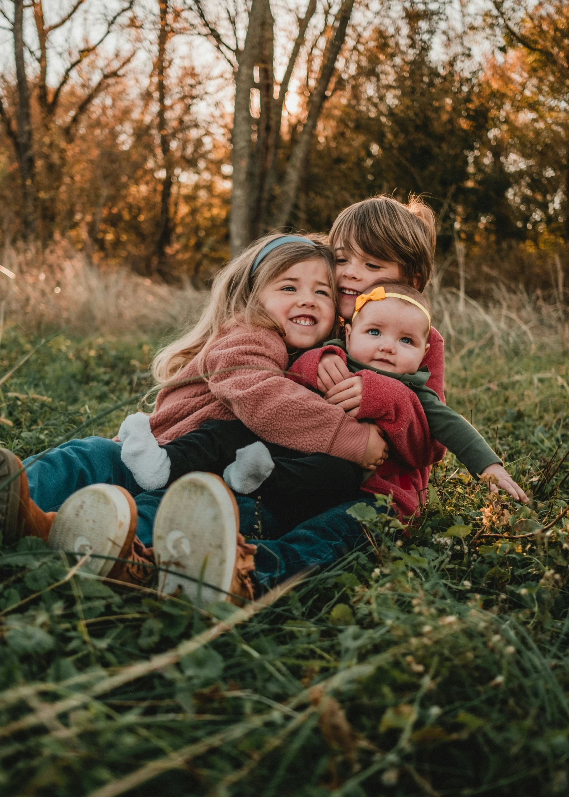 Three children playing together in a grassy field, smiling and embracing, representing joy and safety in a nurturing environment.