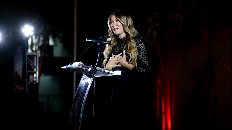 Nia Vardalos speaking at a fundraising event for the Center for the Rights of Abused Children, expressing heartfelt reflections in a supportive atmosphere.
