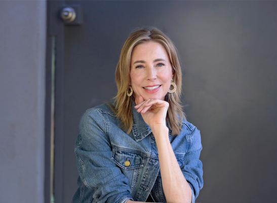 Darcy Olsen, smiling and wearing a denim jacket, poses thoughtfully with her hand on her chin, reflecting her advocacy for the rights of abused children.