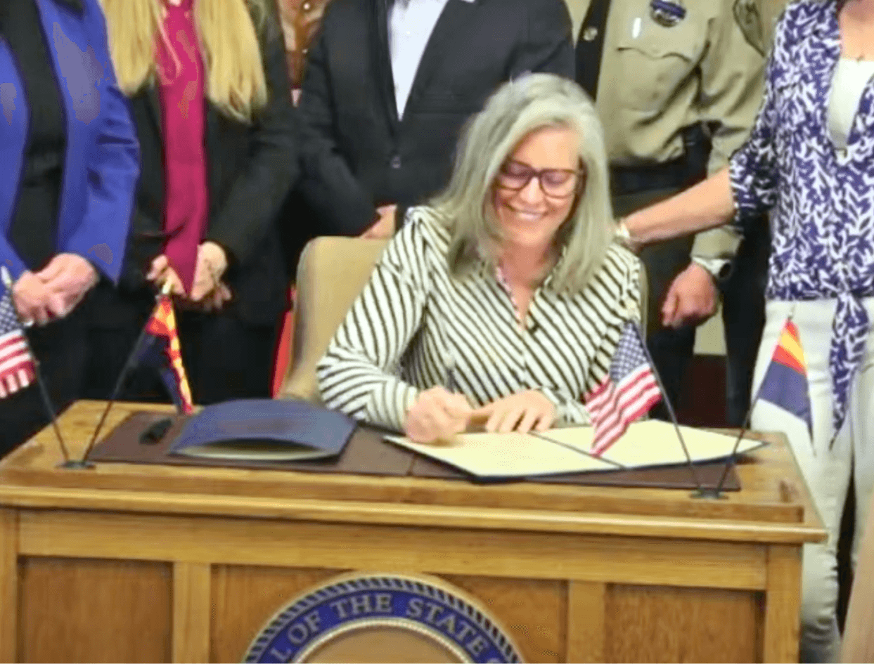Governor Katie Hobbs signing child safety reform bill with flags and supporters present, enhancing transparency and oversight of the Department of Child Safety in Arizona.