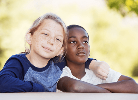 Two children, a Caucasian boy with freckles and a Black boy, sitting closely together, smiling and posing for the camera, symbolizing friendship and support in the context of child welfare and family reunification efforts.