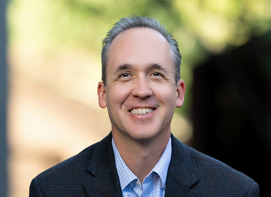 Tim Keller, smiling in a professional setting, featured in context of child welfare advocacy and efforts to reduce state care duration for abused children.