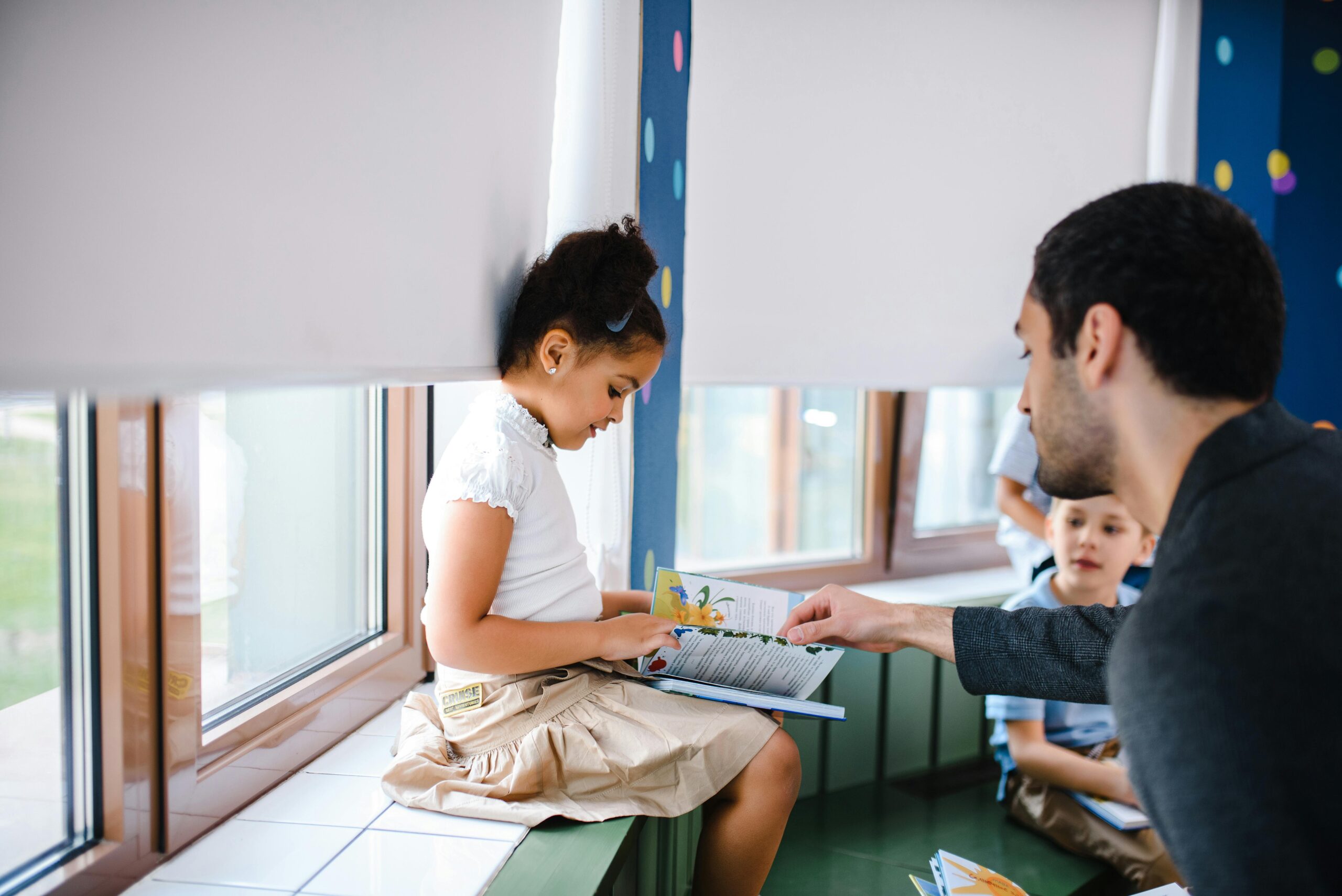 Child reading in a classroom with adult assisting, emphasizing educational support and engagement for children in need.