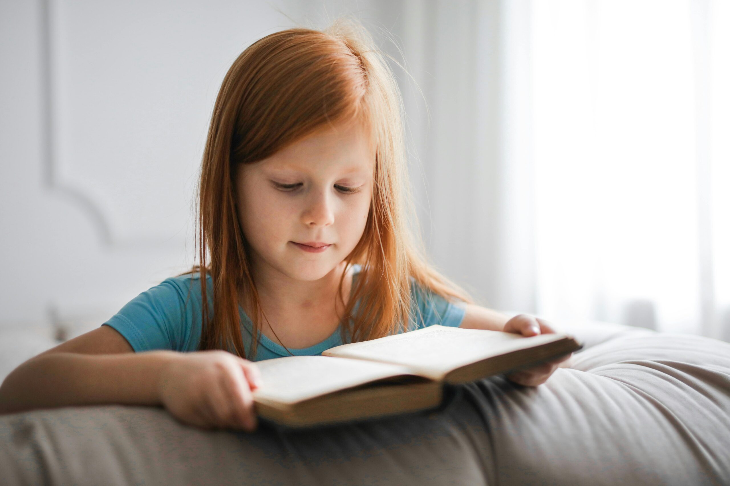 Girl reading a book on a couch, symbolizing the importance of education and support for foster children&rsquo;s rights.