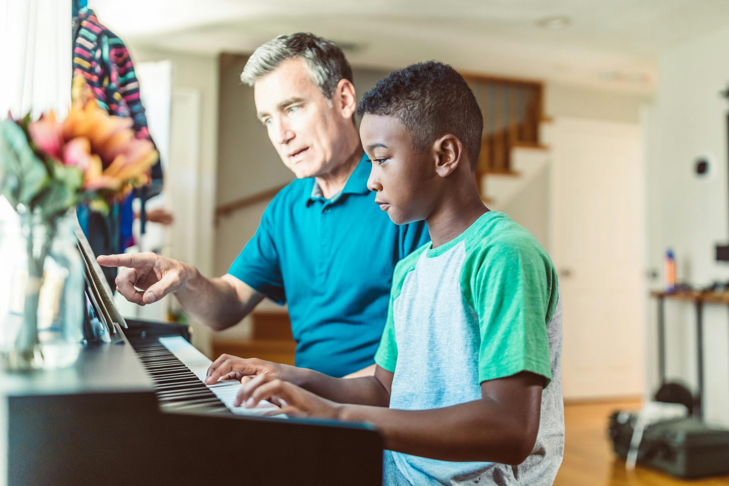 Man teaching a boy to play piano, emphasizing mentorship and connection, relevant to National Adoption Month and supporting children in need.