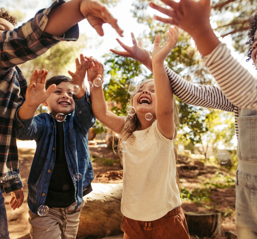 Children joyfully reaching for bubbles outdoors, highlighting the importance of stable environments for educational success in foster care.